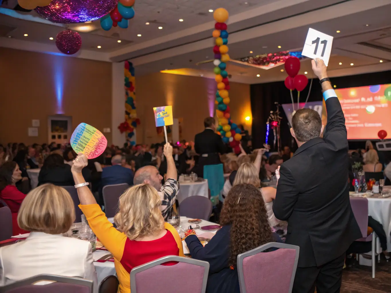 A vibrant, high-resolution photograph capturing the excitement of an art auction, with attendees bidding on a colorful abstract painting. The scene is set in a well-lit auction hall, emphasizing the energy and prestige of the event.